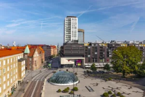 En stadsmiljö med moderna och äldre byggnader, en glasstruktur och spårvägar.