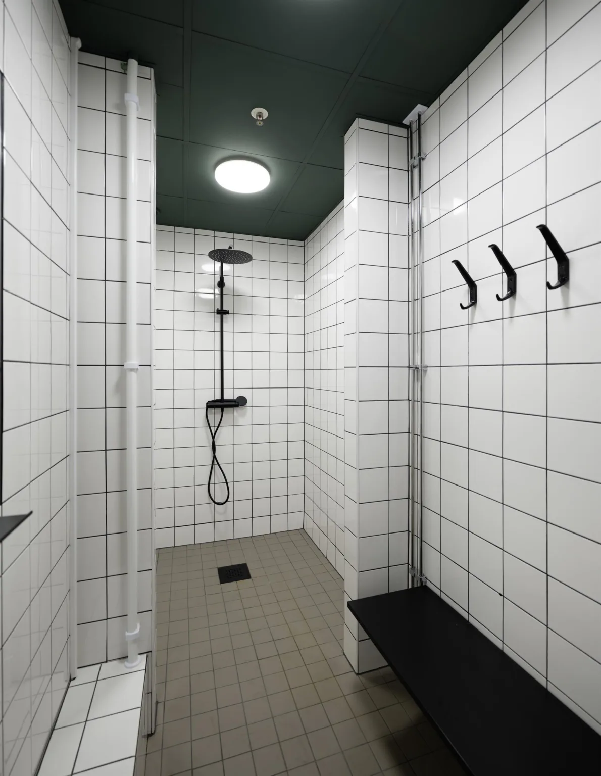 3. Duschutrymme med vita kaklade väggar, mörkt tak, duschmunstycke och krokar på väggen.