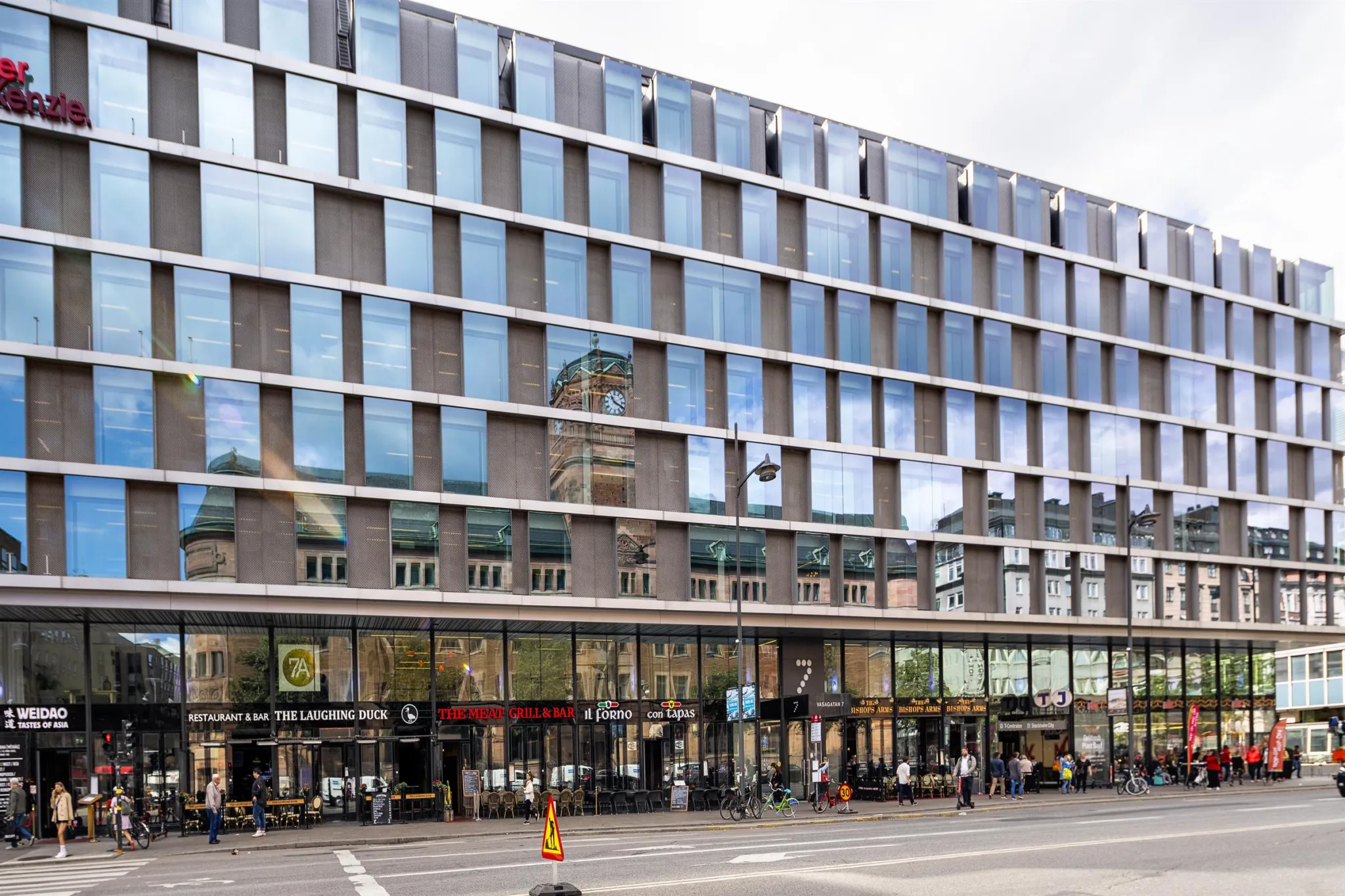 En modern byggnad med glasfasad och flera våningar, med butiker på bottenvåningen.