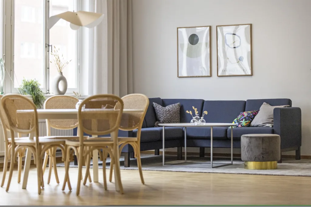 En modern inredning med en matplats och en soffhörna, inklusive trästolar, ett blått hörnsoffa och två tavlor på väggen.