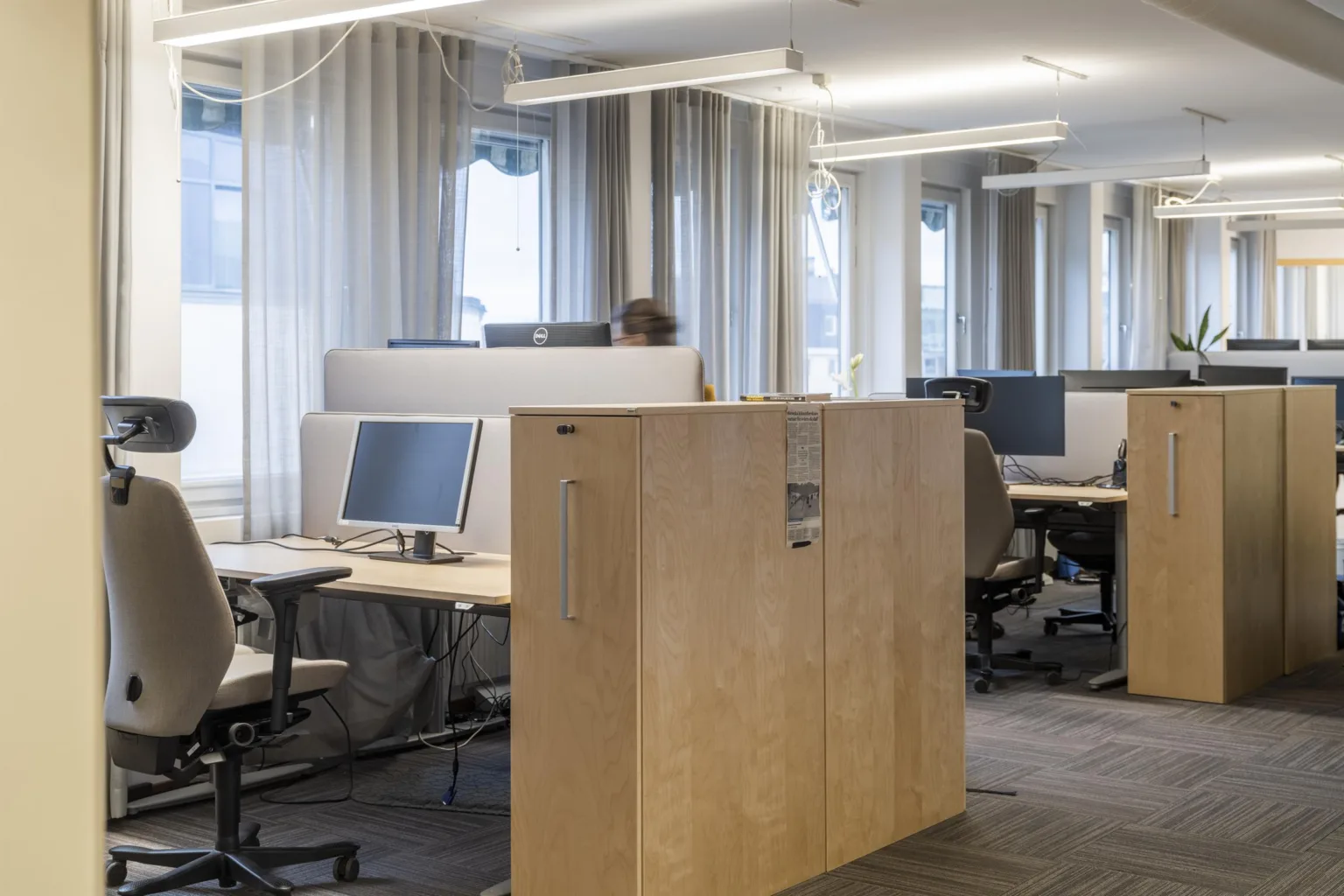 En kontorsmiljö med flera arbetsstationer, datorer, stolar och en träskåp som delar rummet.