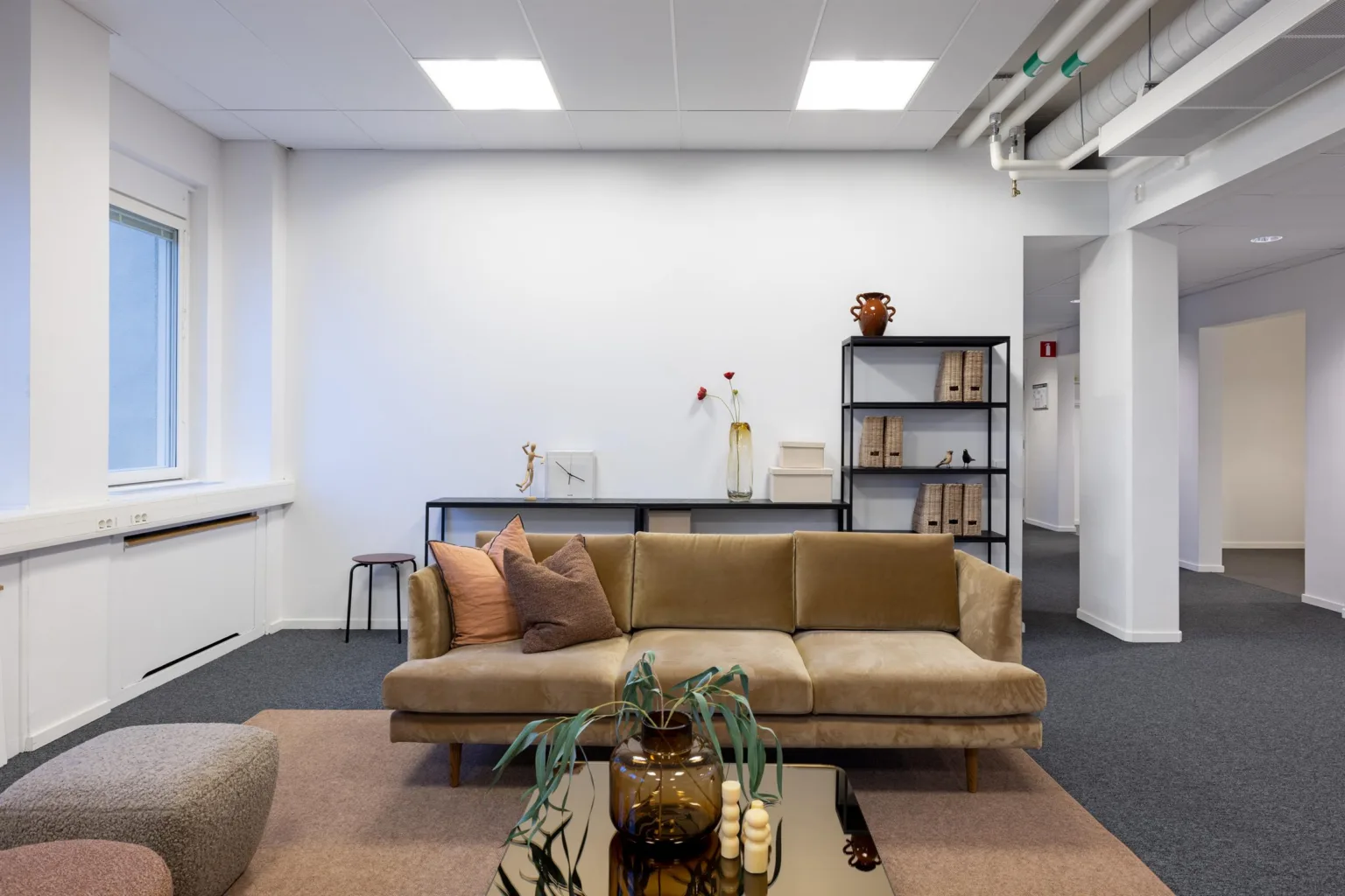 Ett vardagsrum med en beige soffa, soffbord och hyllor med dekorativa föremål i bakgrunden.