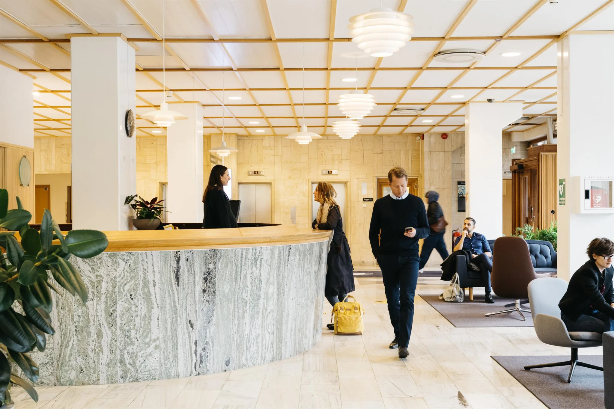Reception med marmordisk i ett öppet och ljust väntrum, människor står och sitter.