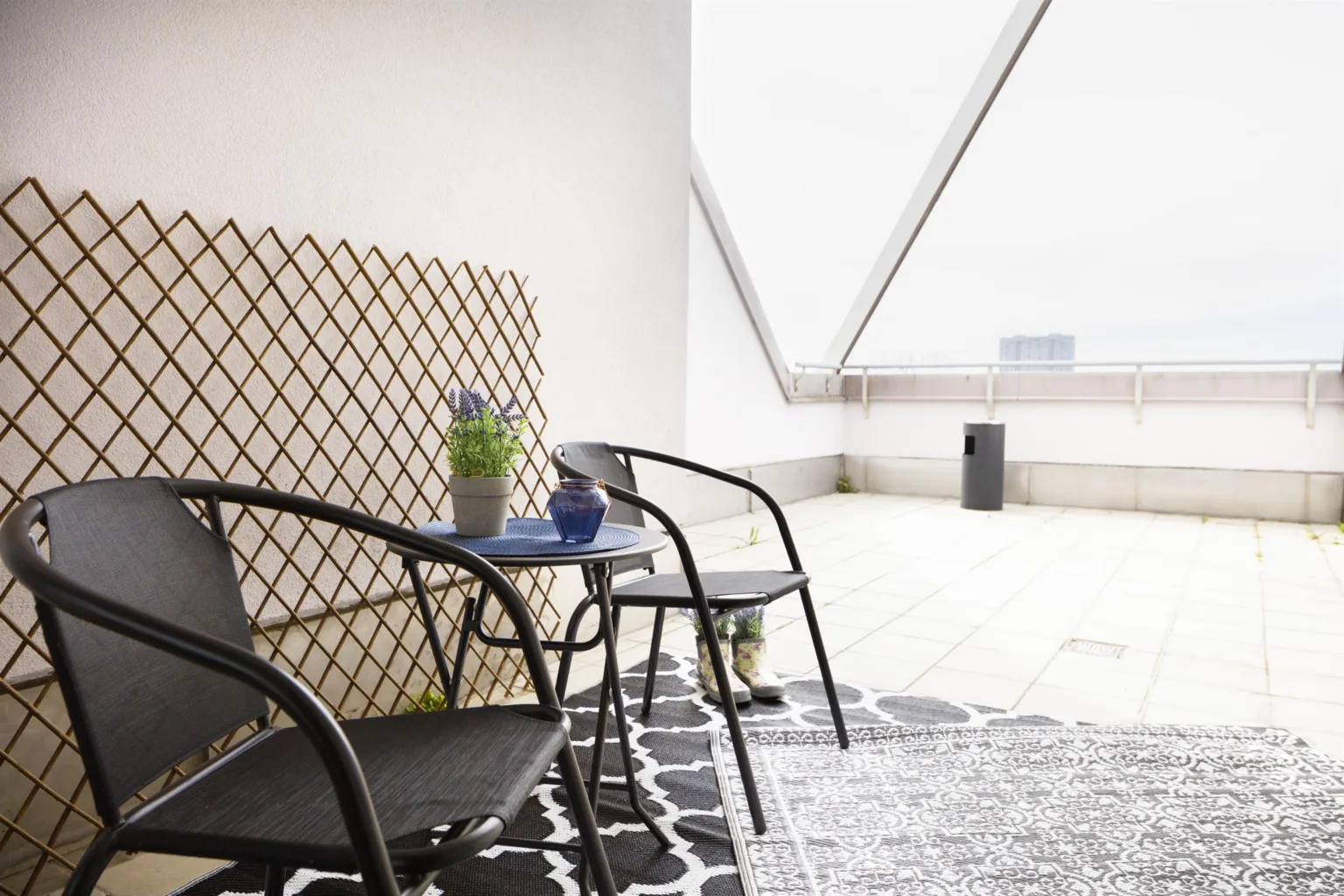 En uteplats med två svarta stolar, ett litet bord, en klätterspaljé och en modern design.