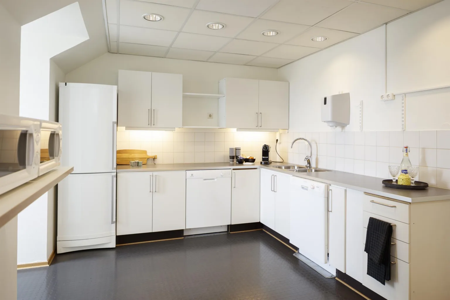 Ett modernt kök med vita skåp, rostfria bänkar och standard köksutrustning, i ett ljust och rent utrymme.
