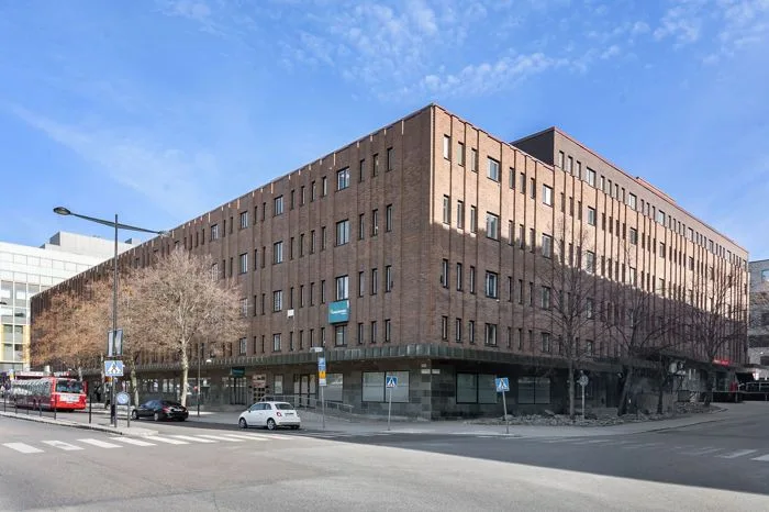 4. En tegelbyggnad i flera våningar vid ett gatuhörn med parkerade bilar och blå himmel.