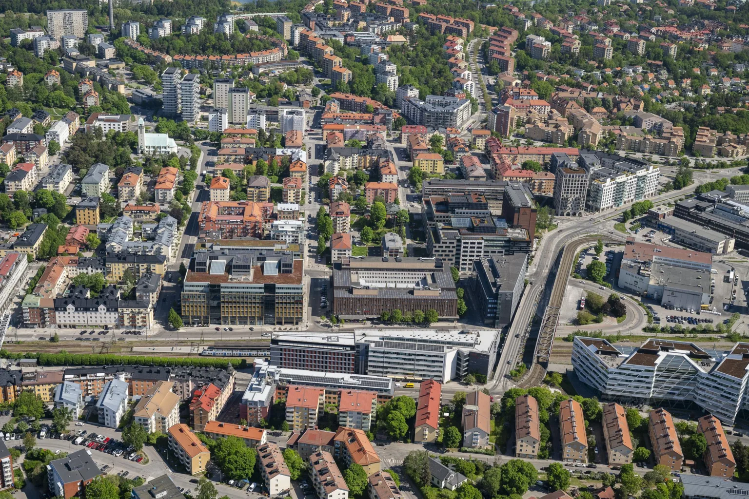 1. Flygbild av en stadsmiljö med tätbebyggda områden, byggnader och vägar omgivna av grönområden.