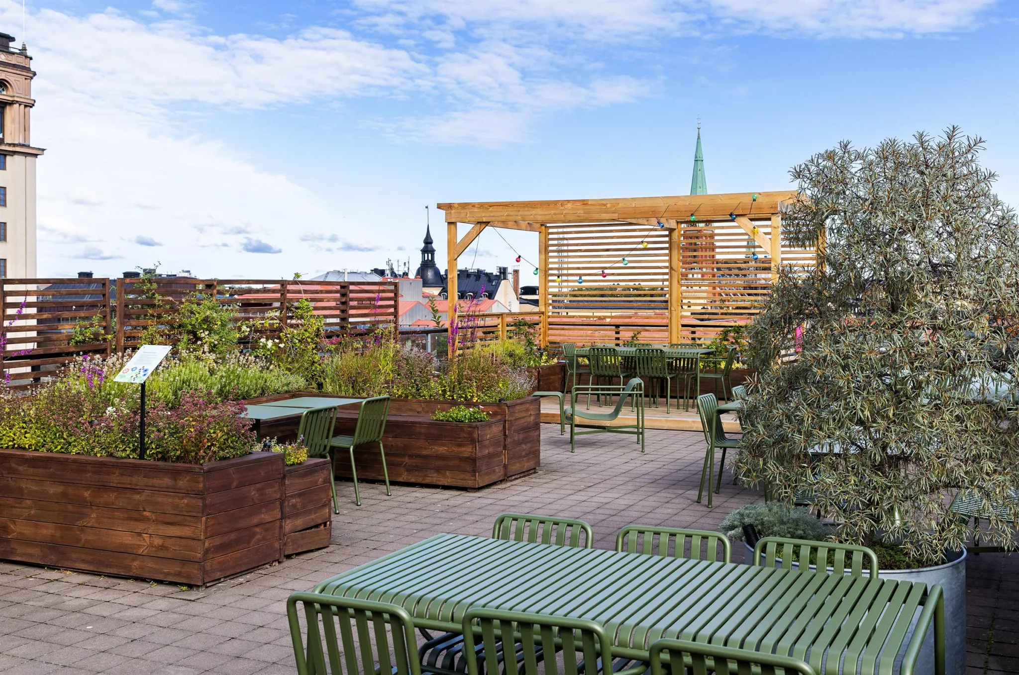 En takterrass med flera sittgrupper, växtlådor och utsikt över stadens byggnader.