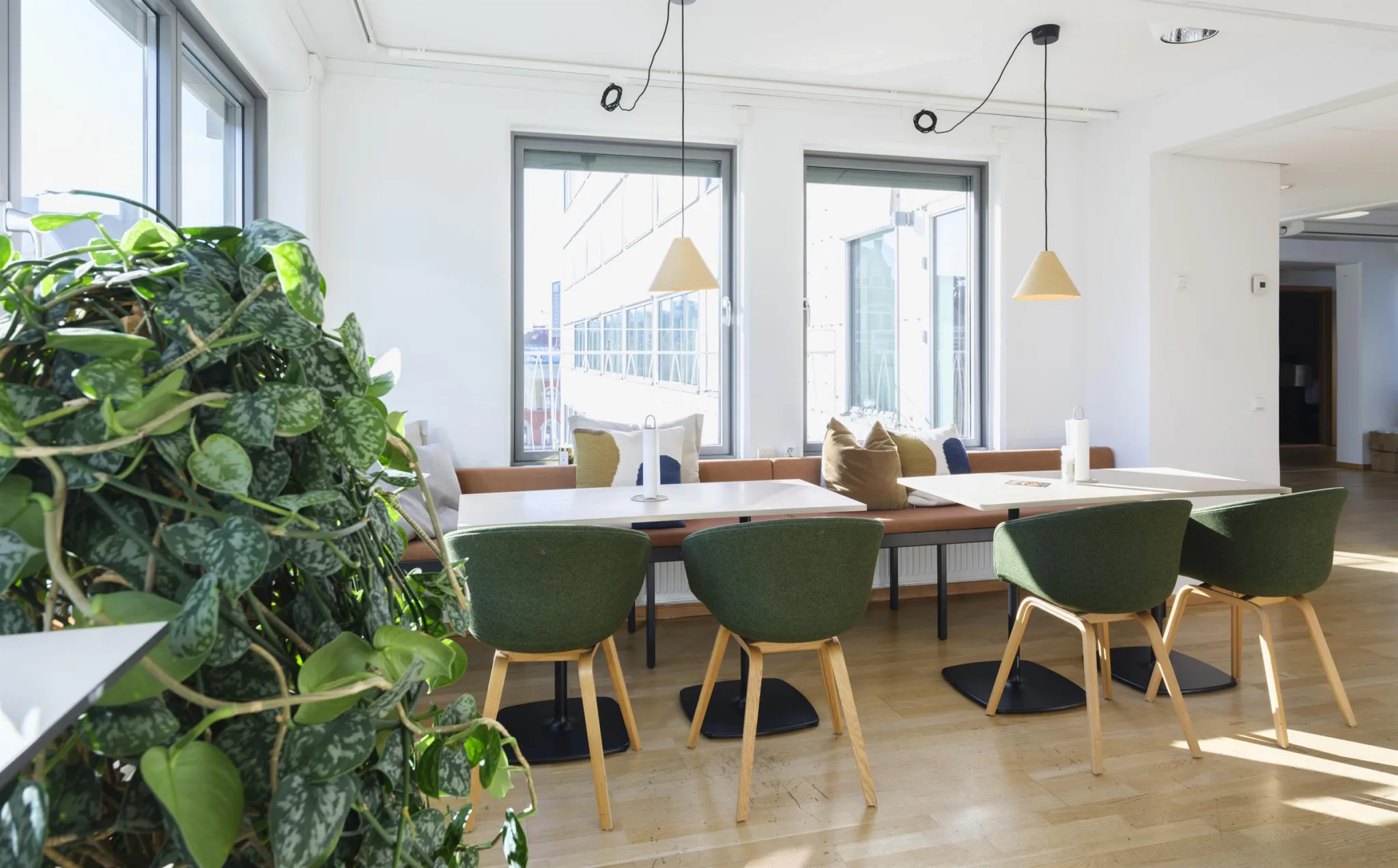 4. Ett gemensamt utrymme med långa bord, gröna stolar och dekorativa hängande lampor, med ett grönt växtarrangemang i förgrunden.
