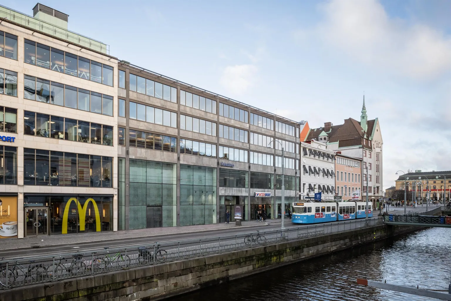 1. En byggnad med glasfasad vid en kanal, där McDonald's och spårvagnsskyltar syns.