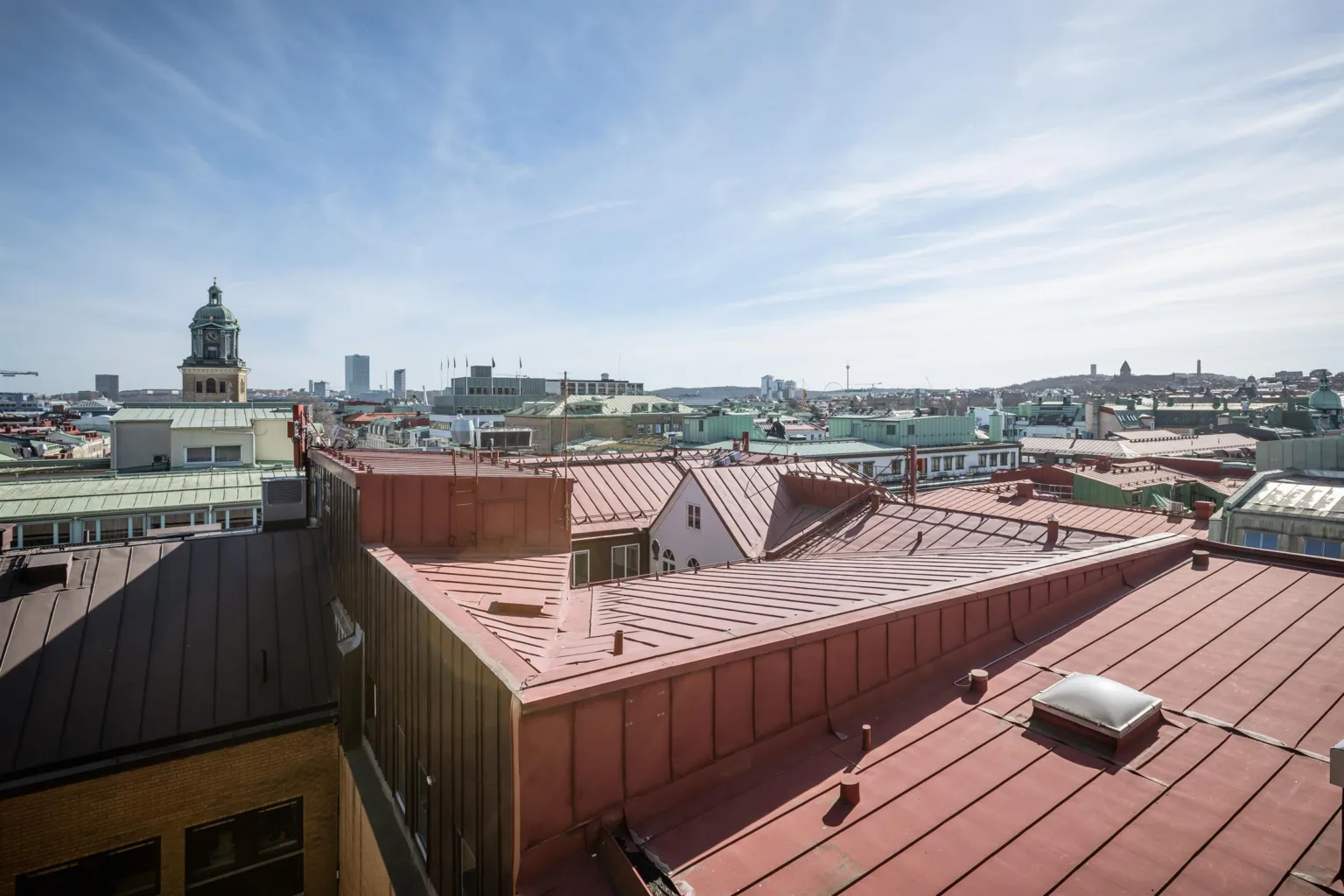 En utsikt över tak i en stad, med röda tak och byggnader under en klar blå himmel.