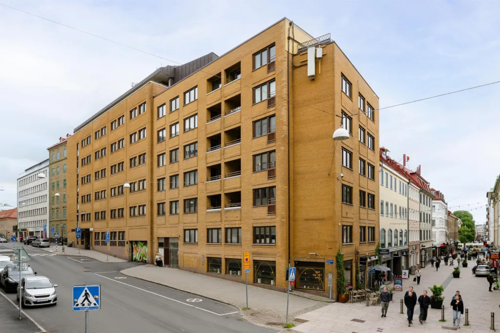 En tegelbyggnad med sex våningar, belägen vid en gata med trottoarer och fotgängare.