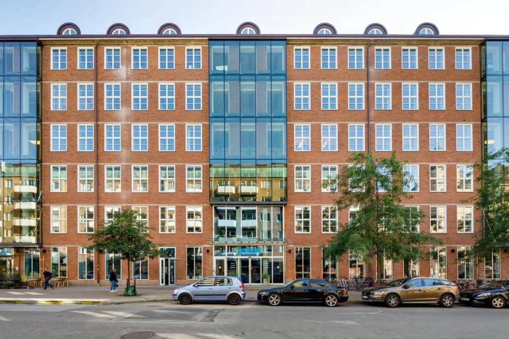 Framsidan av en tegelbyggnad med symmetriska fönster och glaspartier i mitten.