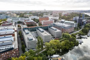 Flygfoto över ett kontorsområde med modern arkitektur, omgiven av grönska och vatten.