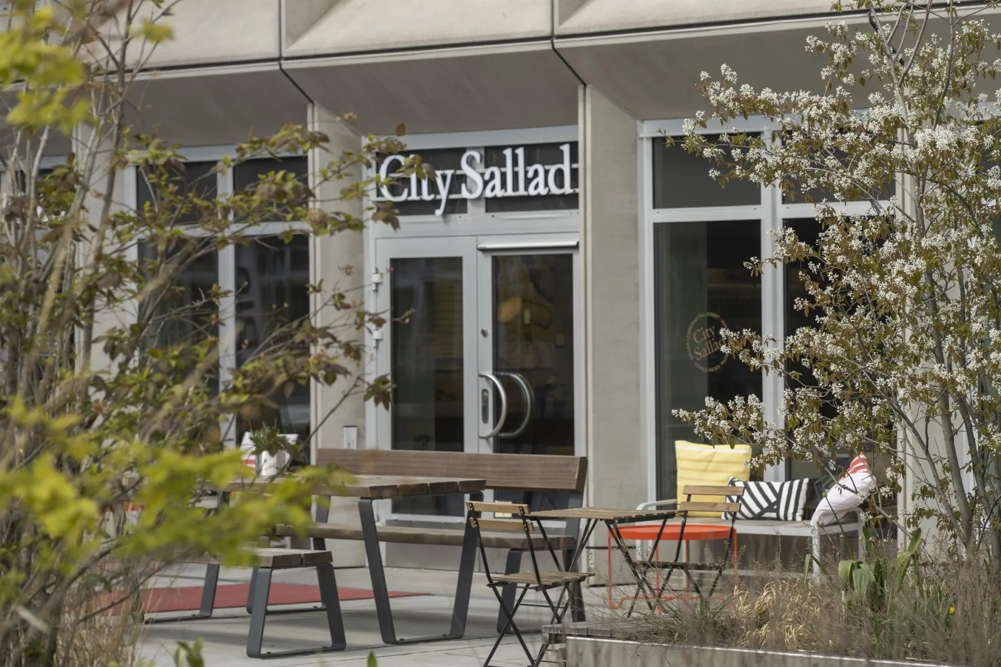 En butik med namnet "City Sallad" på fasaden, utomhusbord och stolar.