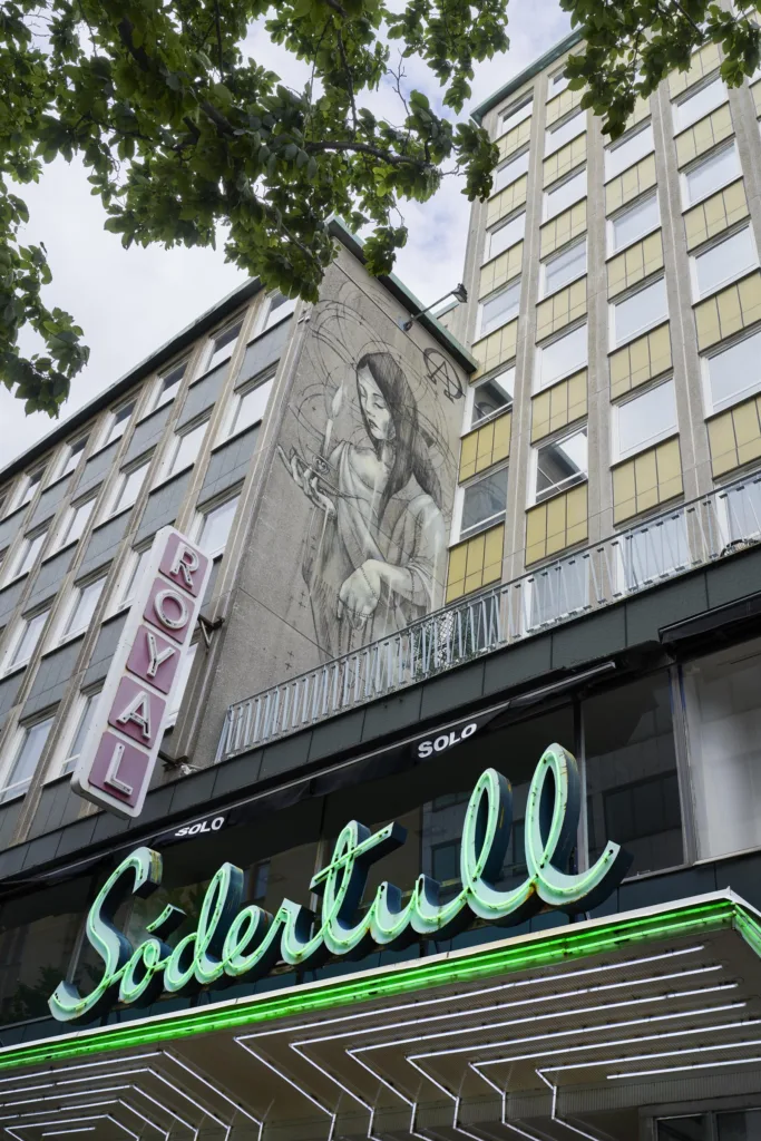 En byggnad med en målning av en kvinna på fasaden, samt en neonskylt med texten "Södertull" och en skylt med texten "Royal".
