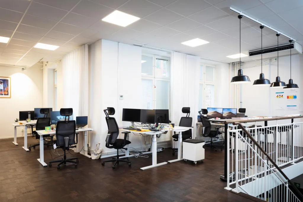 4. Ett öppet kontorslandskap med höj- och sänkbara skrivbord, kontorsstolar och datorskärmar.