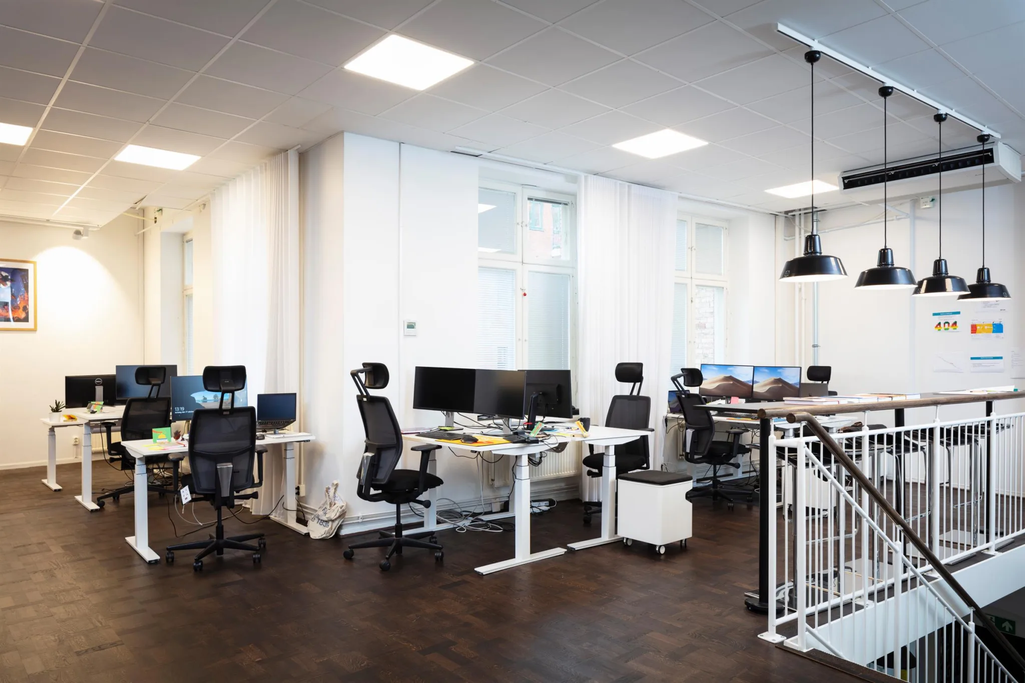 4. Ett öppet kontorslandskap med höj- och sänkbara skrivbord, kontorsstolar och datorskärmar.