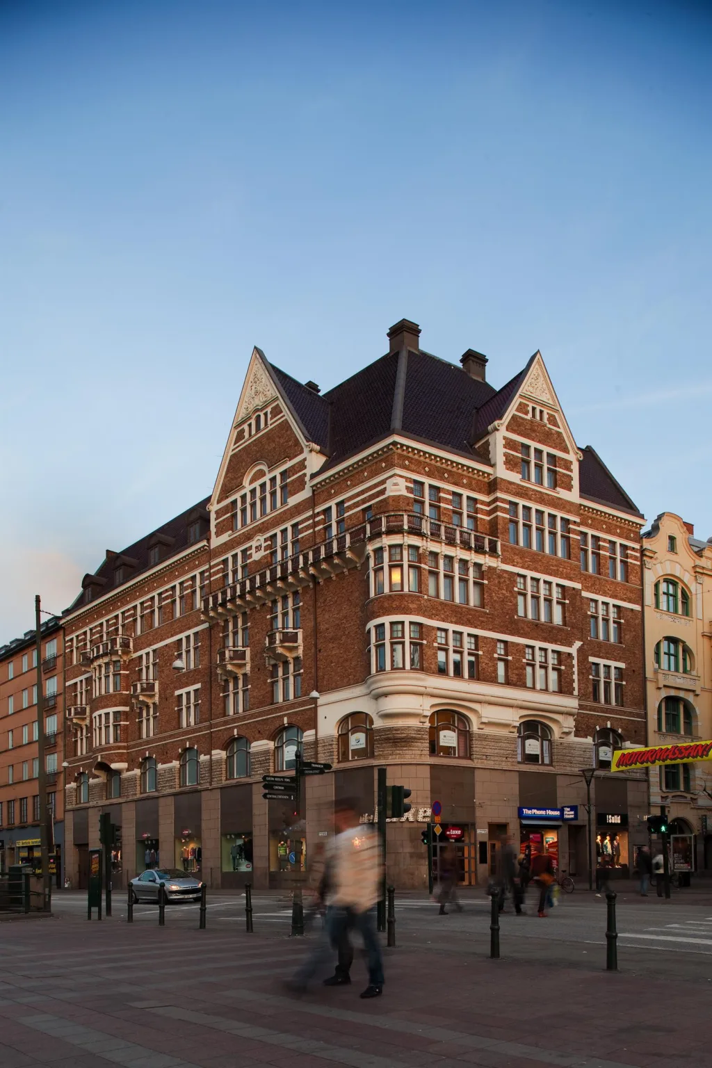 1. En röd tegelbyggnad med spetsigt tak och vit detaljerad arkitektur, omgiven av stadsliv och blå himmel.