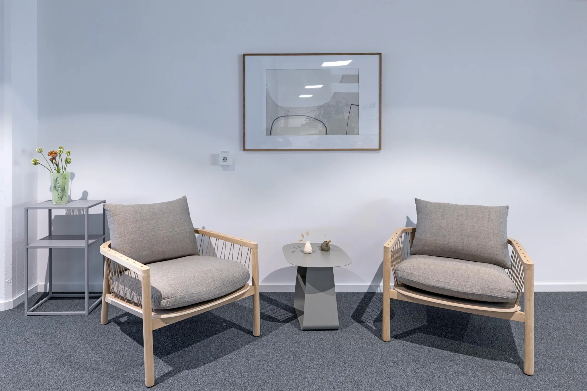 Två bekväma fåtöljer med gråa kuddar står bredvid ett litet bord med en vas. En abstrakt tavla hänger på väggen bakom.