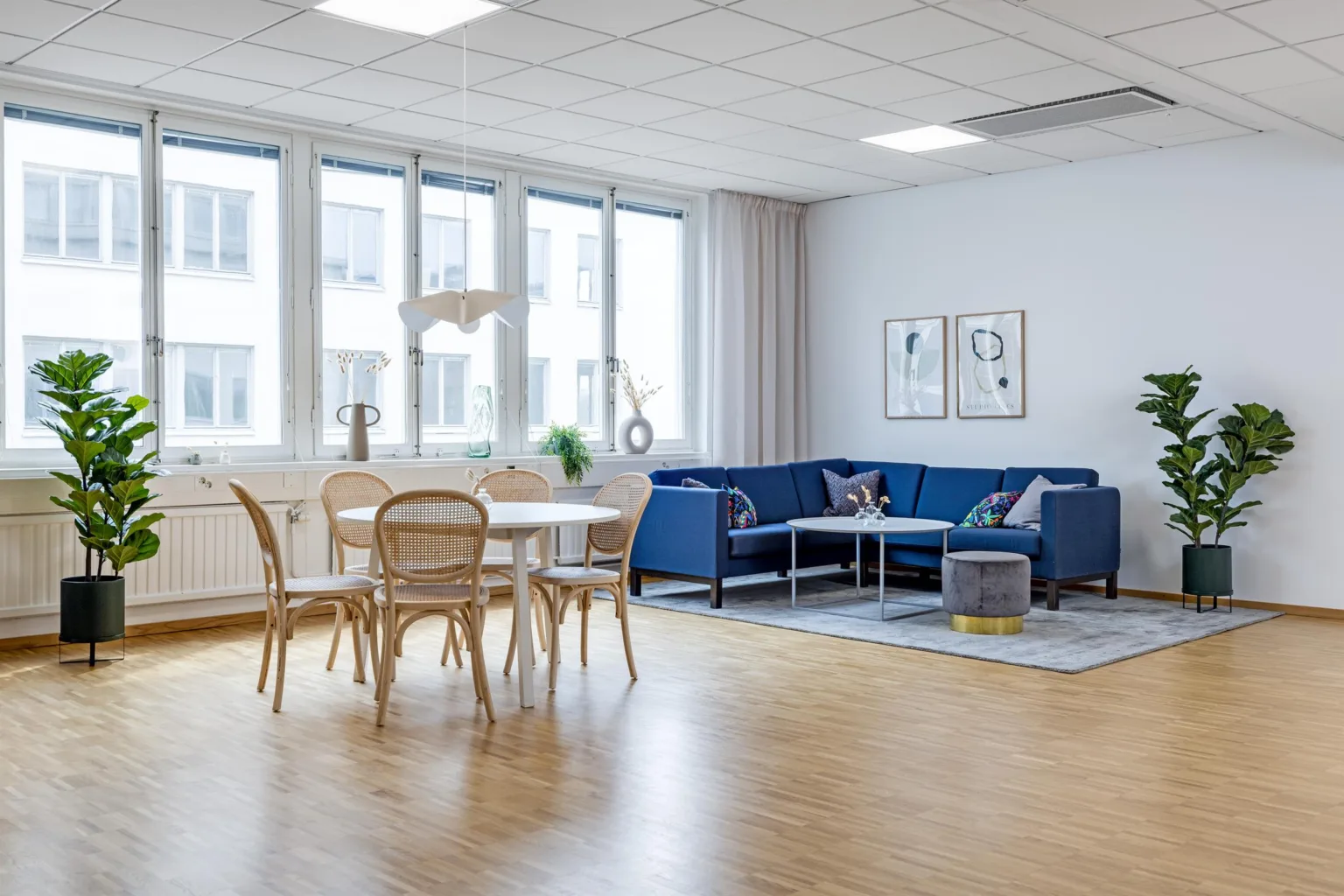 Ett ljust vardagsrum med blå soffa, matbord med stolar och stora fönster.