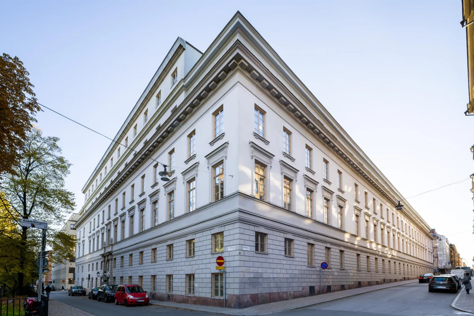 En stor vit hörnbyggnad med klassisk arkitektur och parkerade bilar.