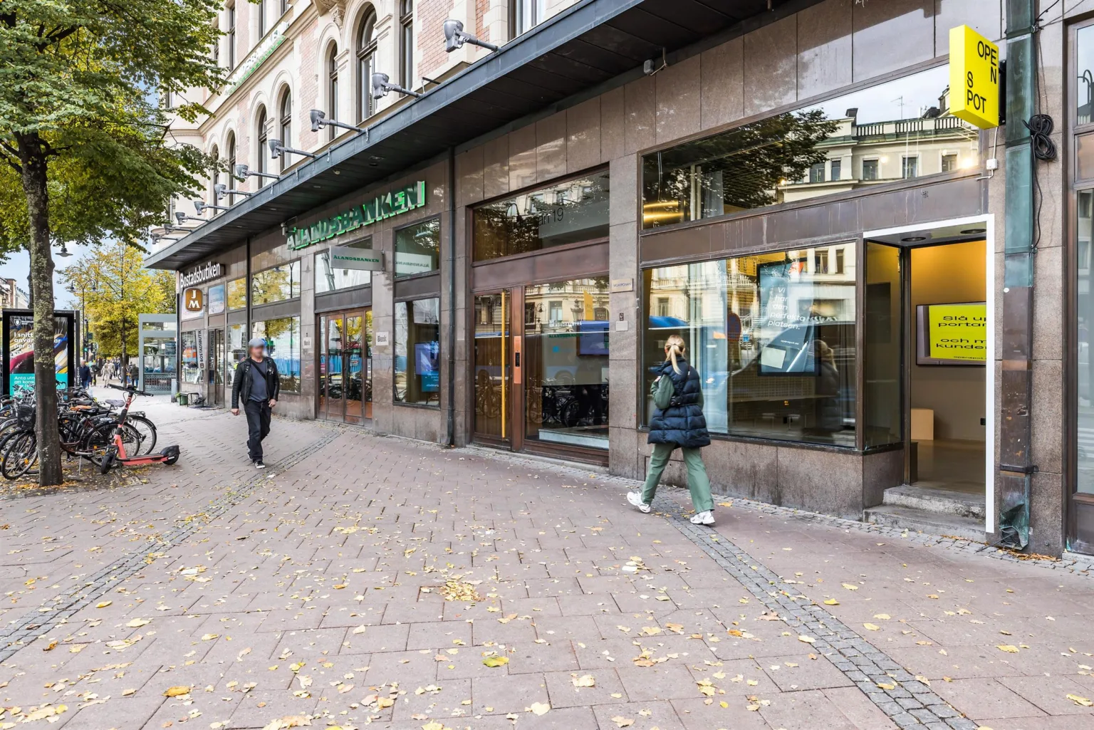 En gata med människor som går förbi en byggnad med stora glasfönster och skyltar.
