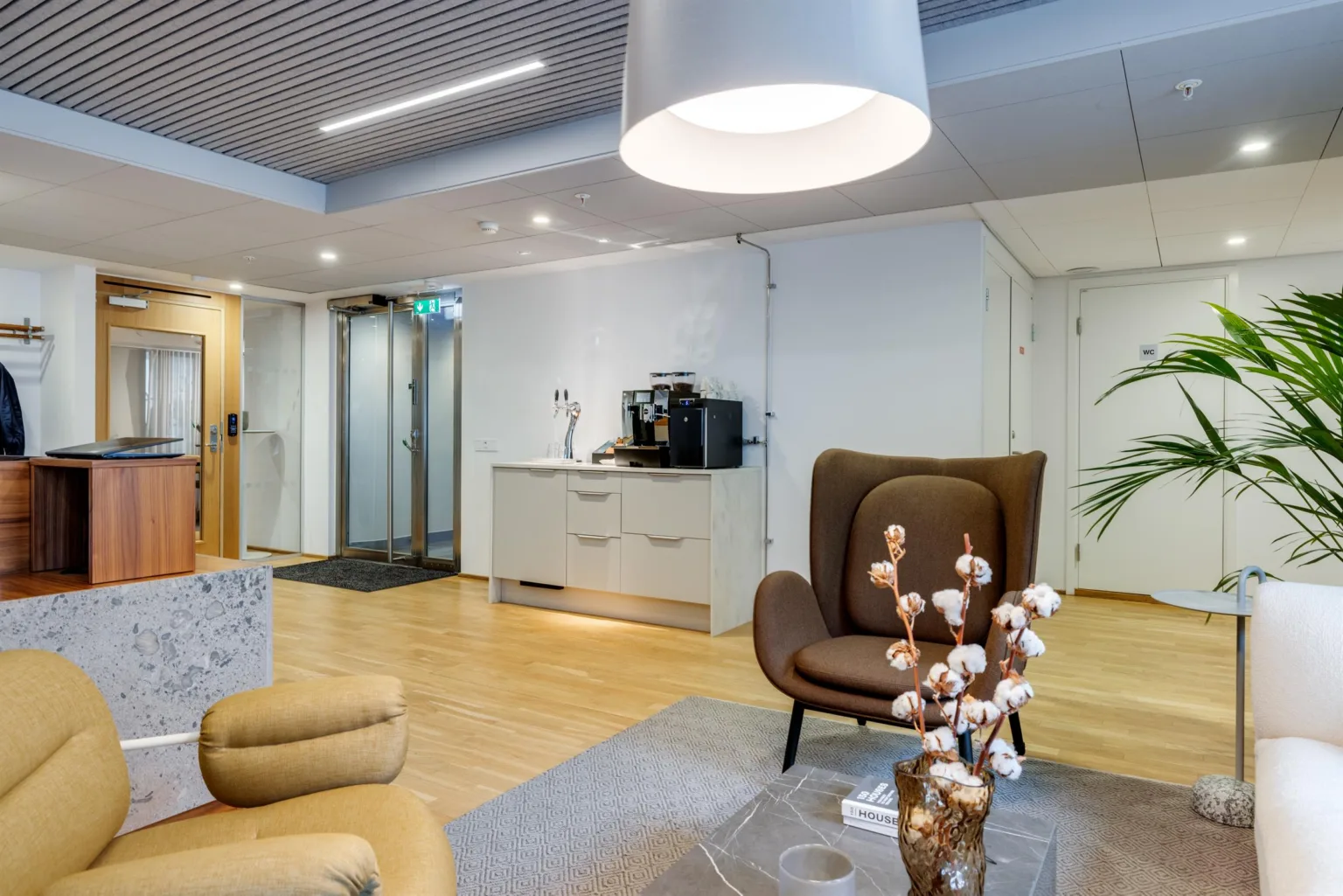 2. Ett väntrum med bruna fåtöljer, en kaffestation och en stor taklampa.