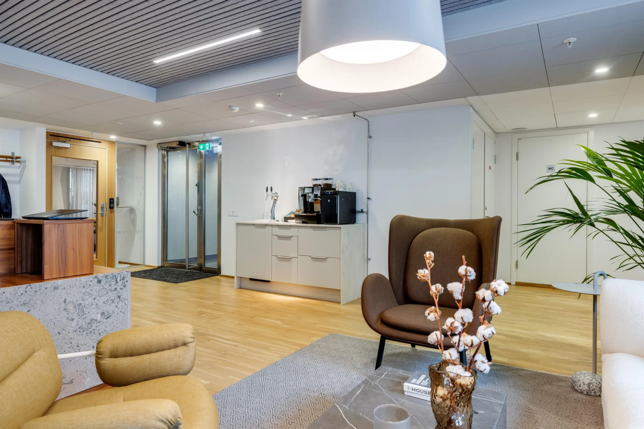 2. Ett väntrum med bruna fåtöljer, en kaffestation och en stor taklampa.
