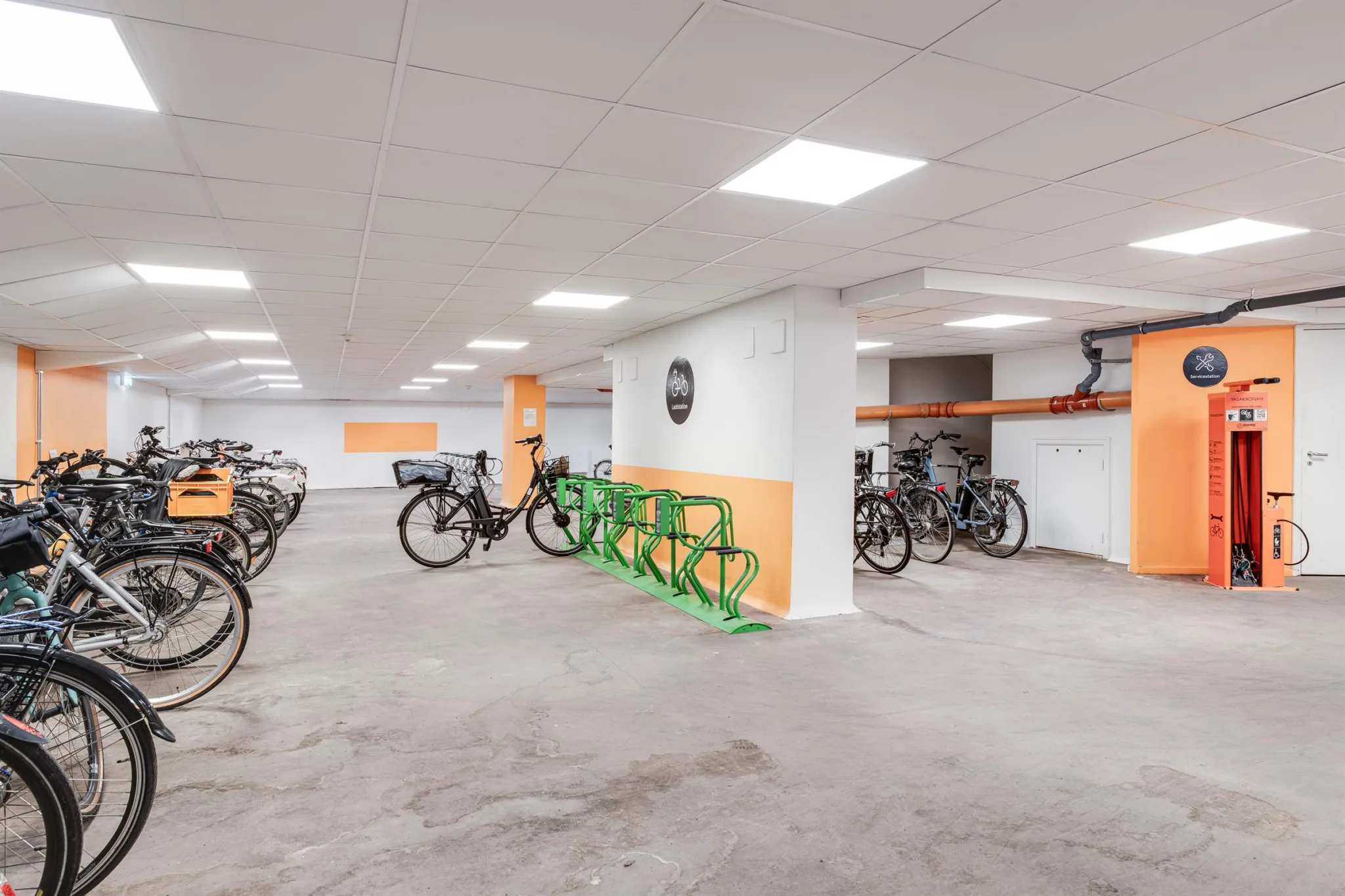 2. Ett cykelförråd med flera parkerade cyklar och gröna cykelställ på en betonggolv.