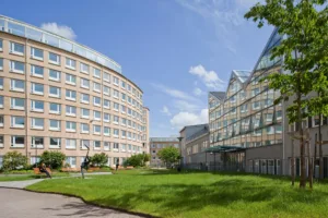 1. Två moderna kontorsbyggnader med glasfasader omgivna av en grön gräsmatta och blå himmel i bakgrunden.