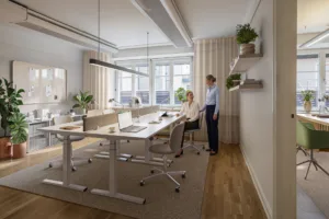 5. Ett kontor med skrivbord, stolar, datorer och två personer som pratar, omgivna av växter och naturligt ljus från fönster.