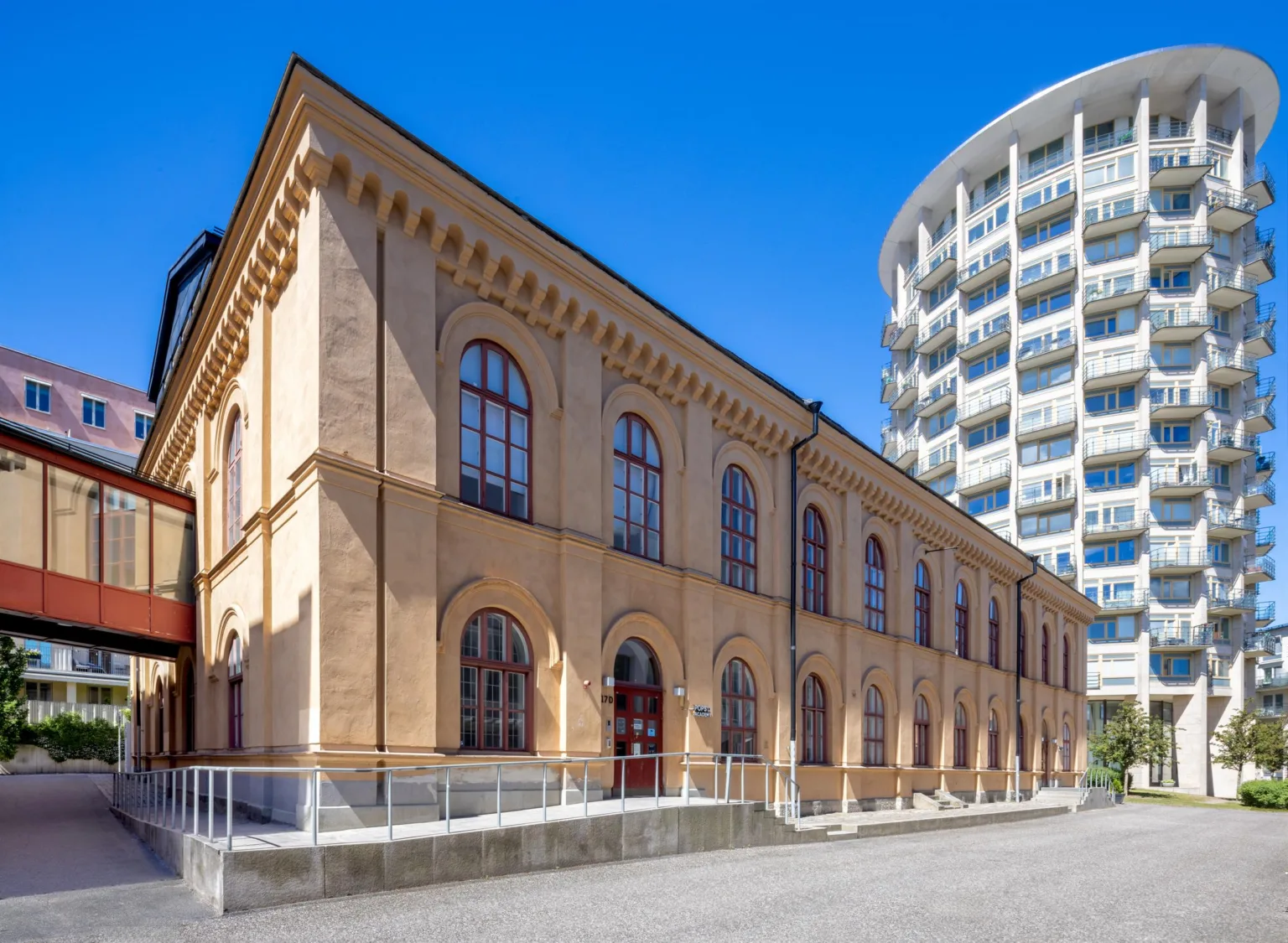 En gammal byggnad med ljusgul fasad och välvda fönster, bredvid en modern vit byggnad med rundad arkitektur.