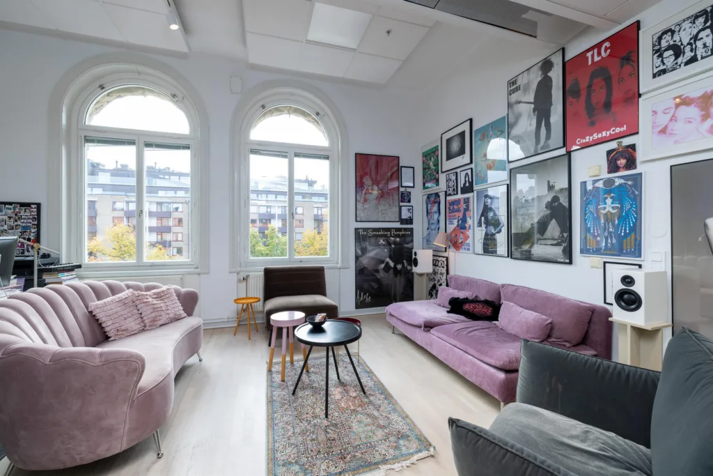 3. Ett vardagsrumsliknande utrymme med rosa soffor, bord och väggar dekorerade med tavlor och affischer.