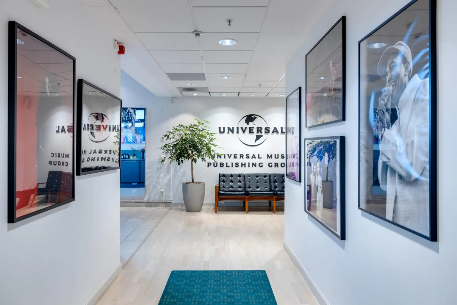 En ljus entré med Universal Music-logotyp på väggen, en soffa och en stor grön växt i hörnet.