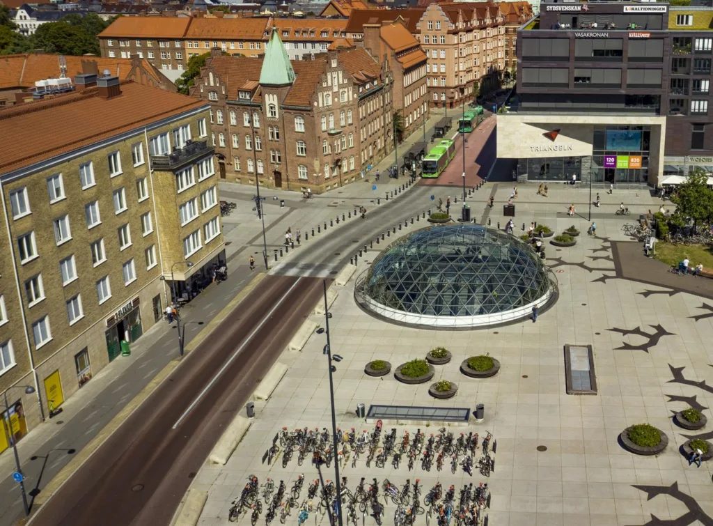 En glaskupol på ett torg omgiven av cykelställ och byggnader med bruna tak.