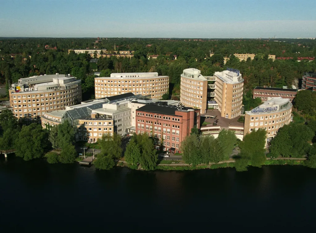 Flygbild av flera byggnader omgivna av träd och vatten.