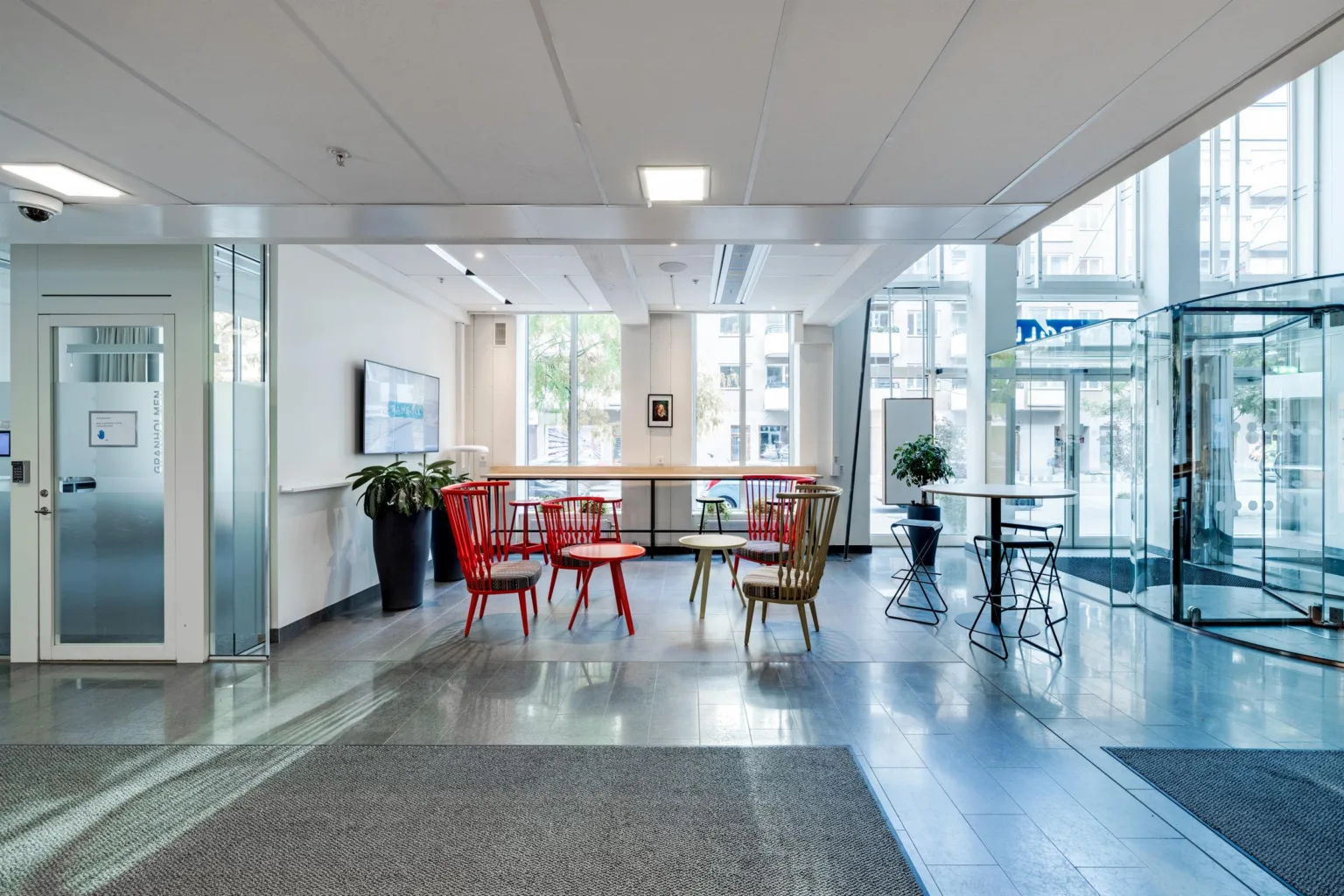 Ett öppet loungeområde med färgglada stolar och bord, stora glasfönster som släpper in dagsljus.