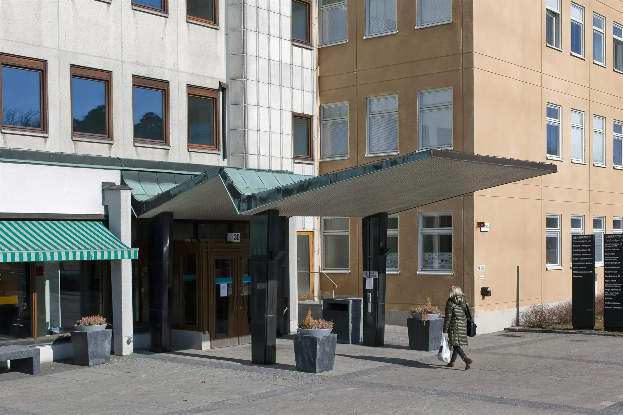 En byggnadsentré med en grön markis, stora fönster och en person som går förbi.