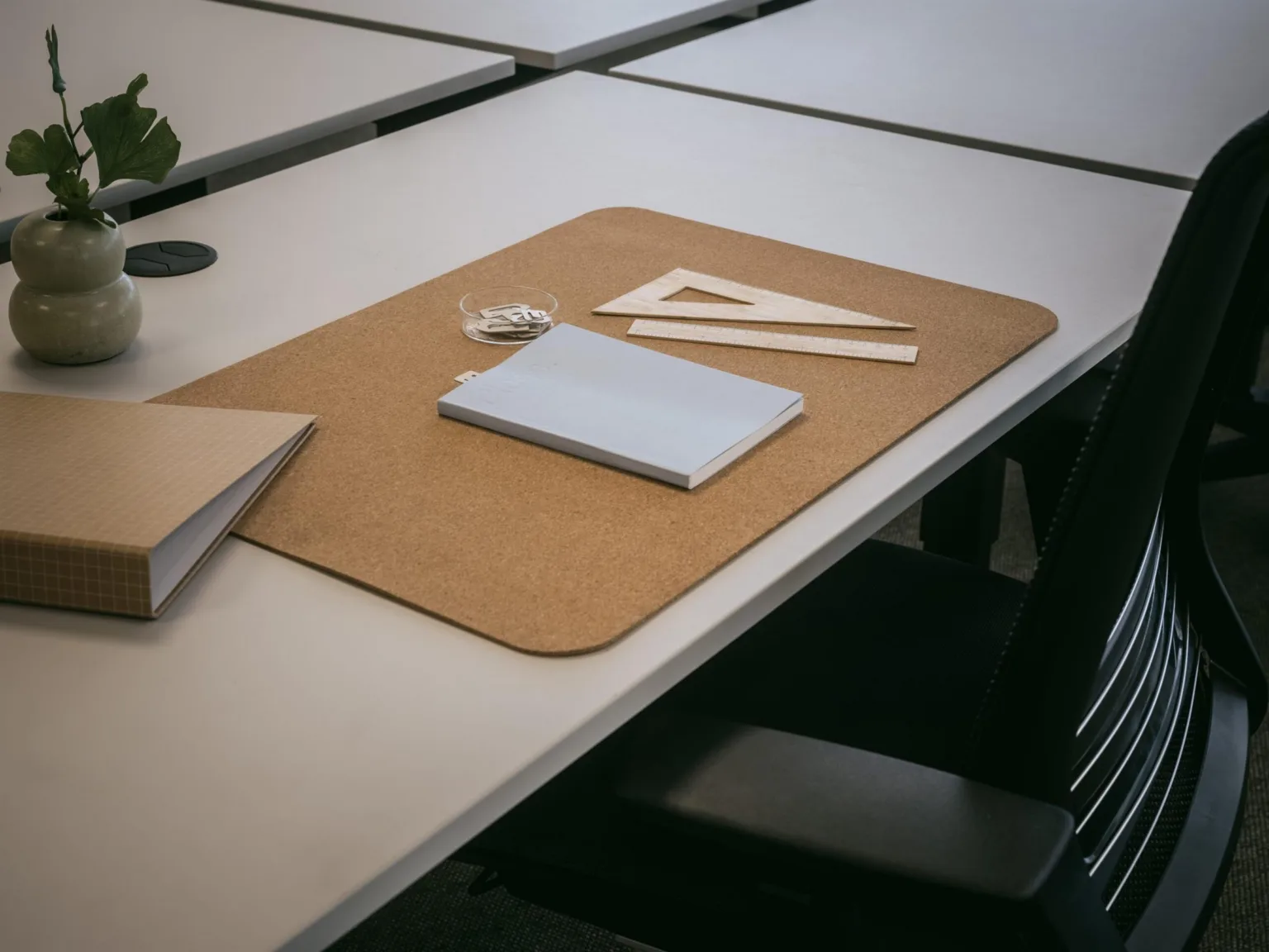 En arbetsyta med en brun skrivbordsunderlägg, anteckningsbok, linjal och geometrisk triangel.