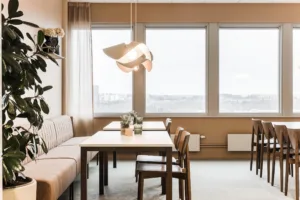 5. En matplats med bord, stolar och en soffa, hängande lampa och stora fönster som släpper in dagsljus.