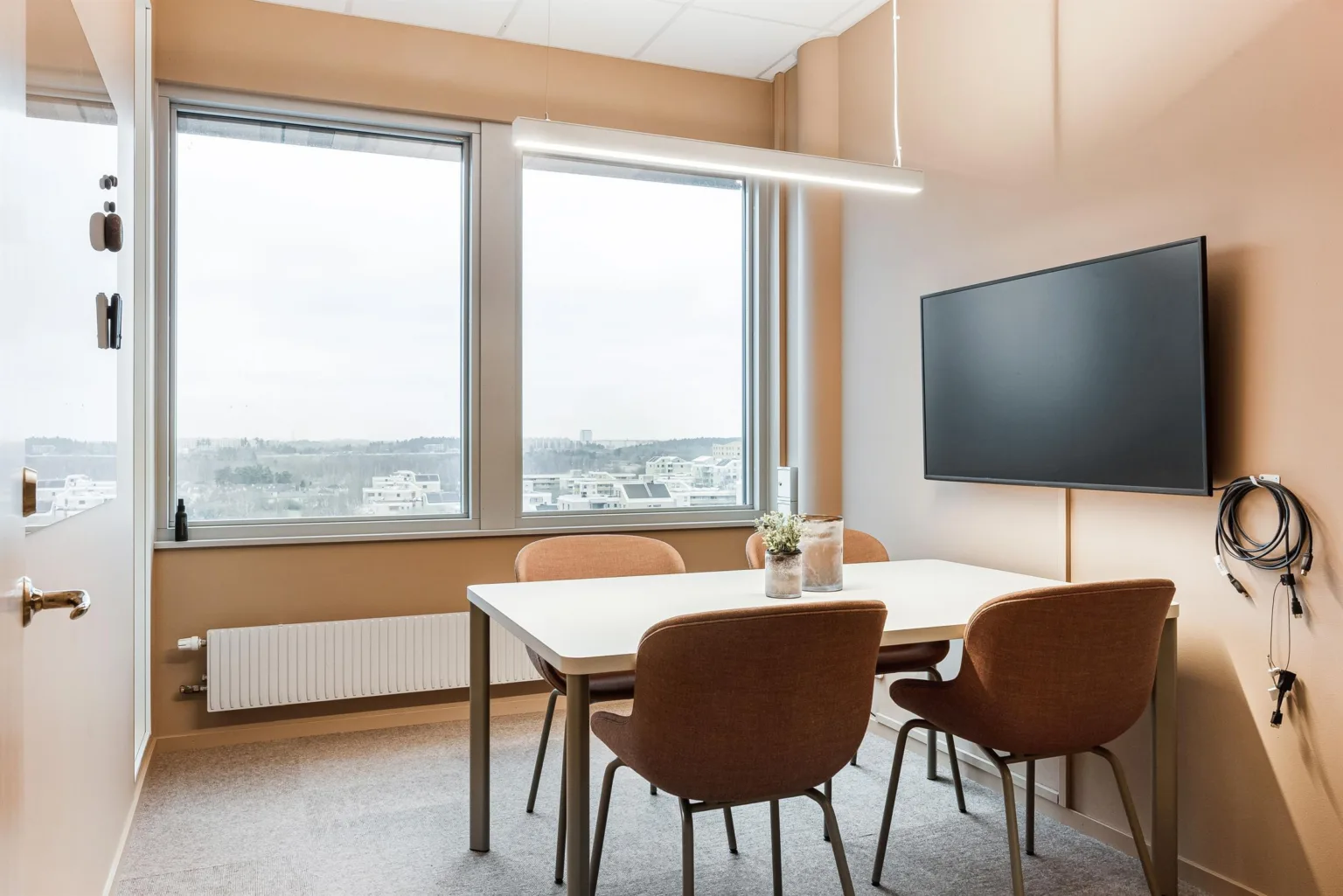 4. Ett mötesrum med bord och fyra stolar, en väggmonterad skärm och ett stort fönster med utsikt.