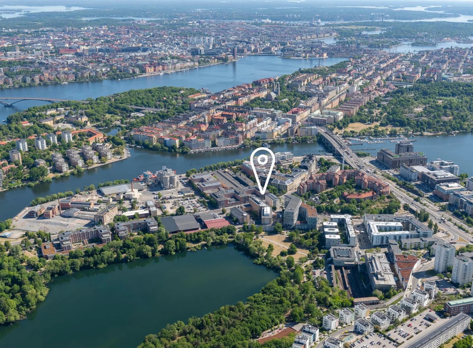 Flygbild över ett stadsområde med sjöar, broar och byggnader. En plats är markerad med en nålikon.