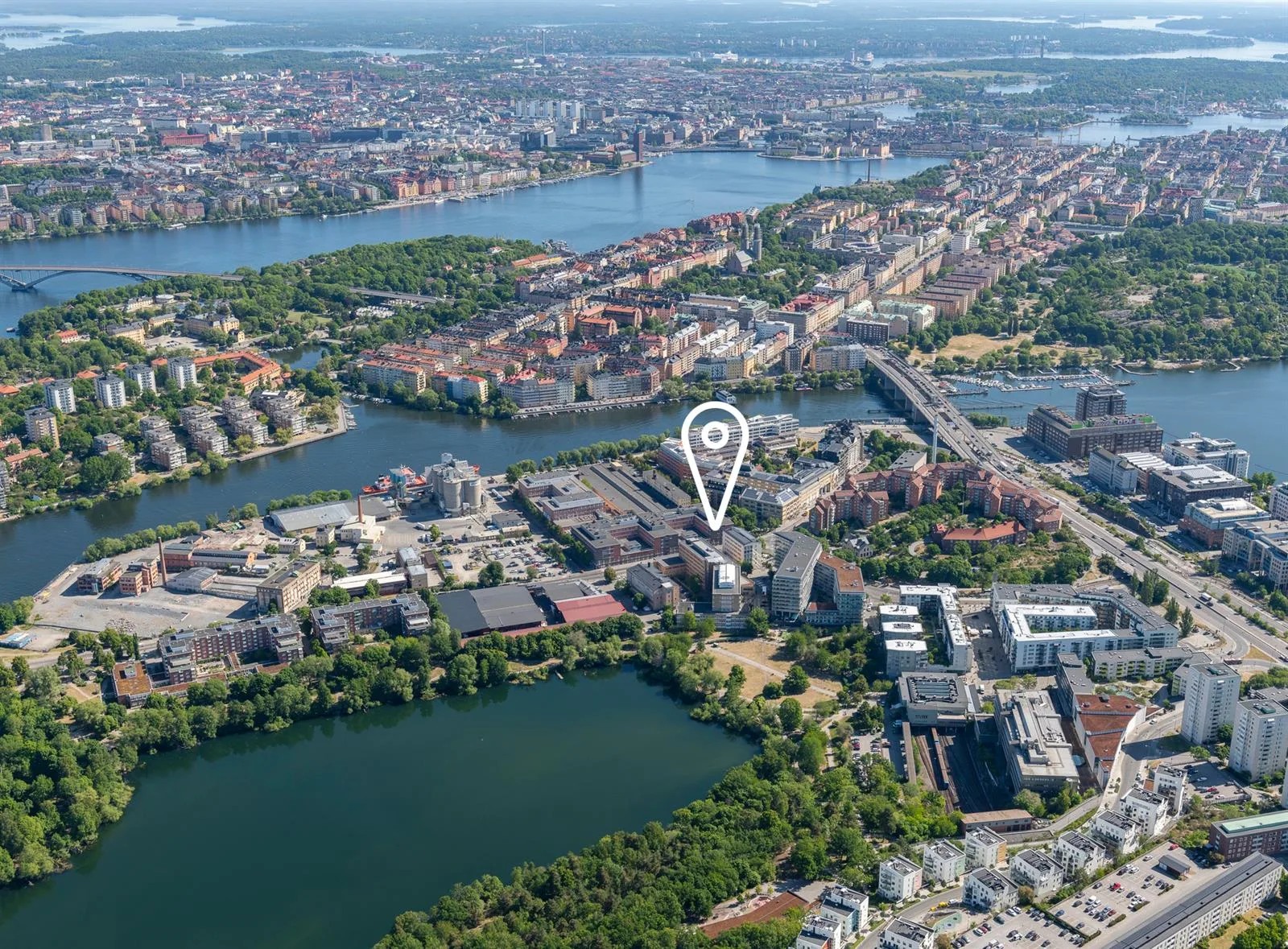 Flygbild över ett stadsområde med sjöar, broar och byggnader. En plats är markerad med en nålikon.