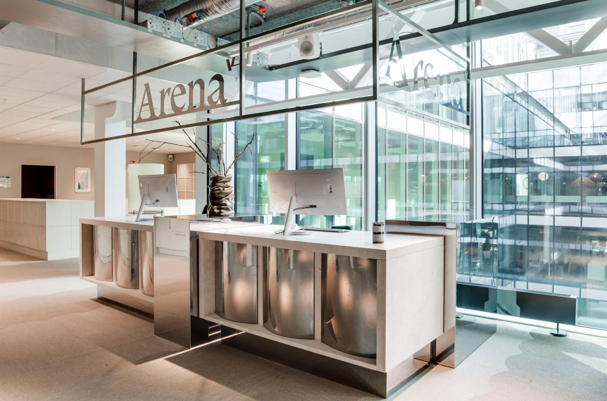 Reception med skylten "Arena" och två datorskärmar, omgiven av glasväggar och modern design.
