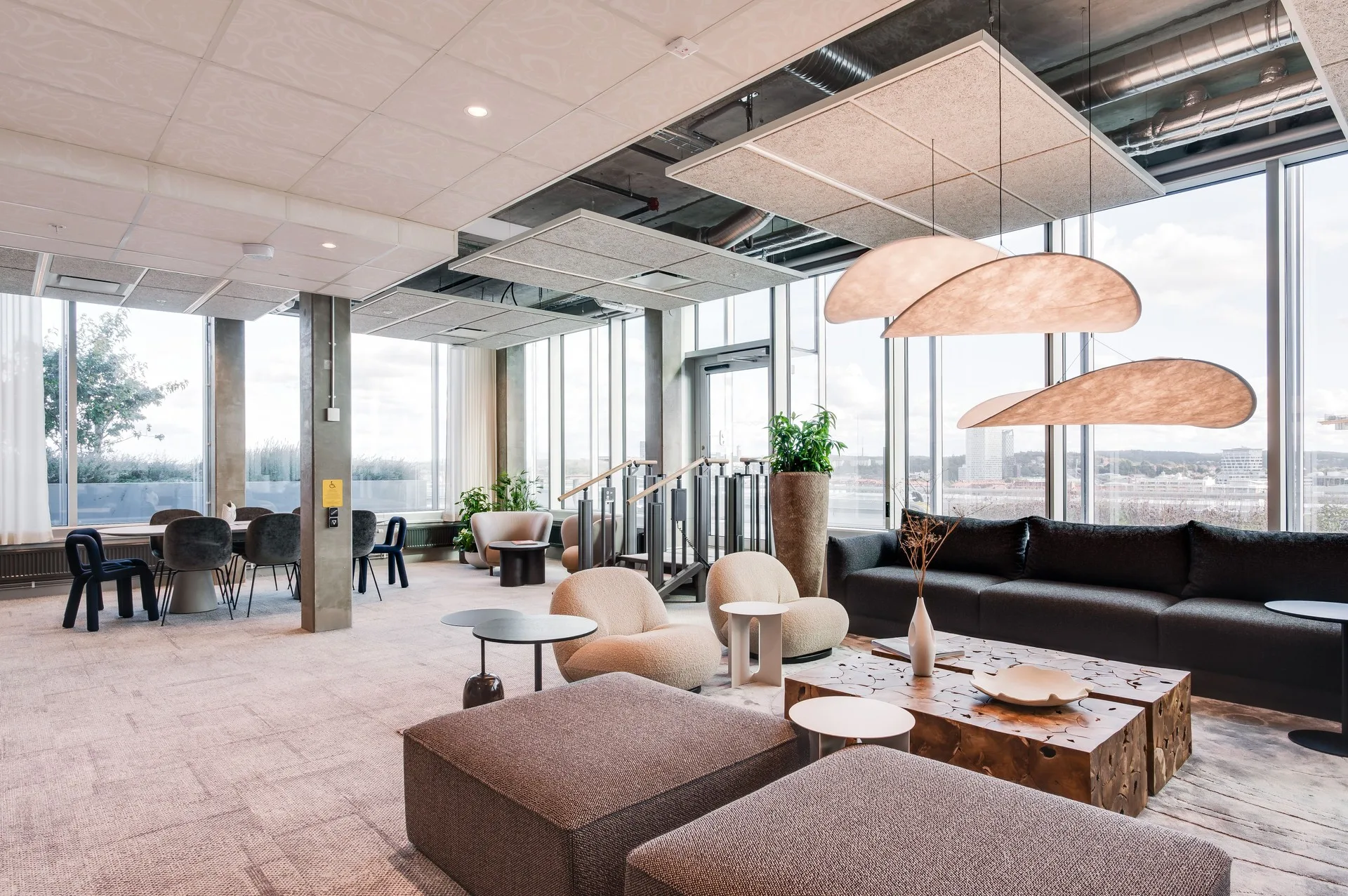 En ljus och rymlig lounge med soffor, bord, växter och stora fönster.