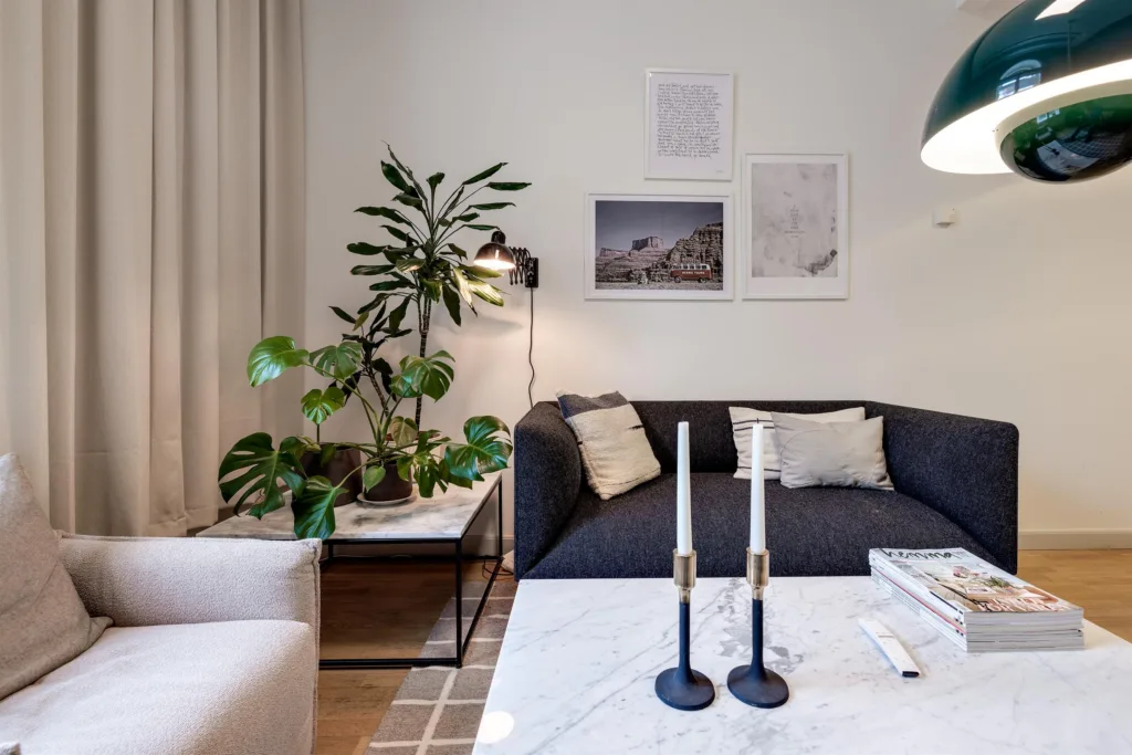En närbild av en sittgrupp med en svart soffa, ett marmorsoffbord med ljusstakar och växter bredvid.