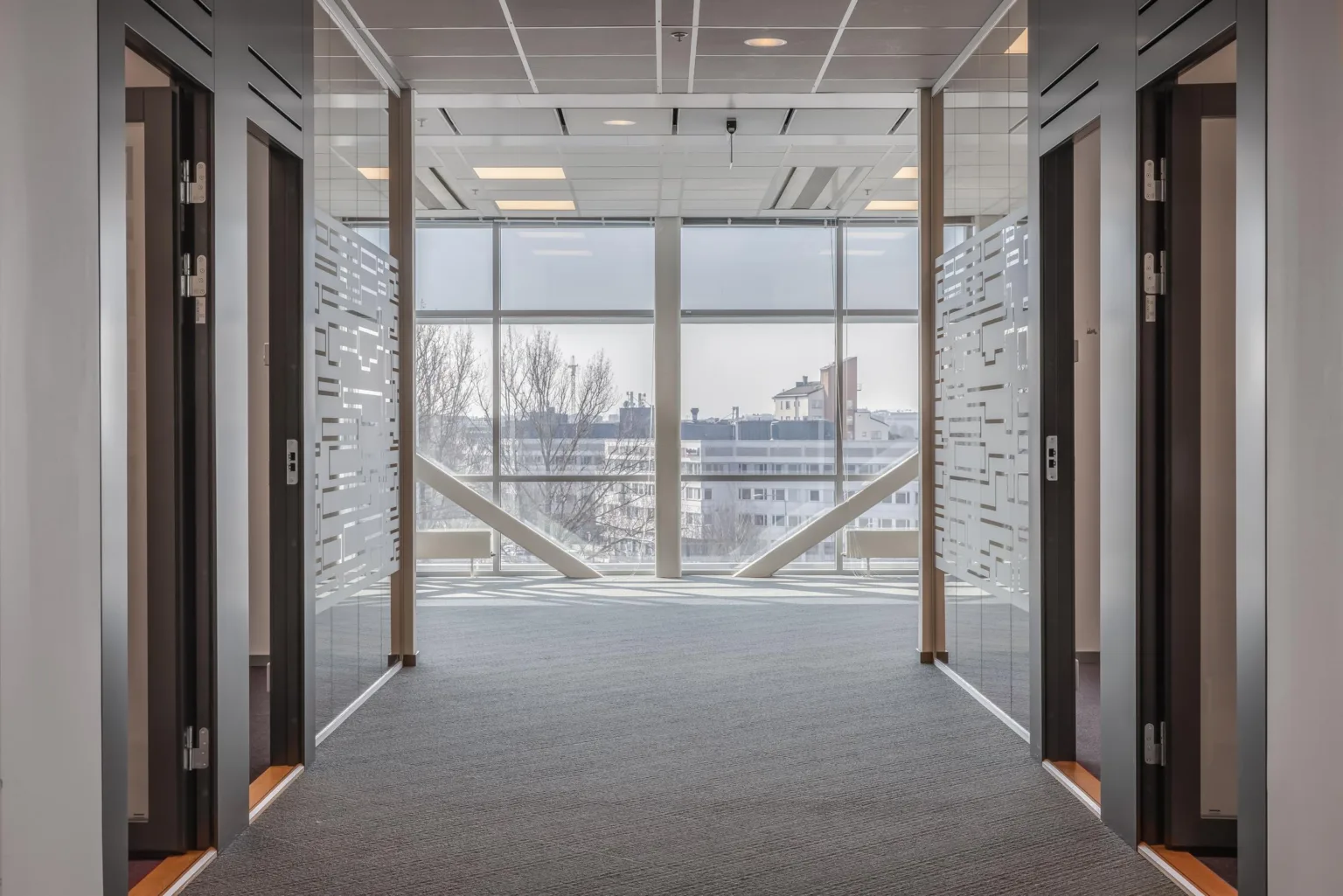 En modern korridor med glasväggar och en utsikt över byggnader genom ett stort fönster.