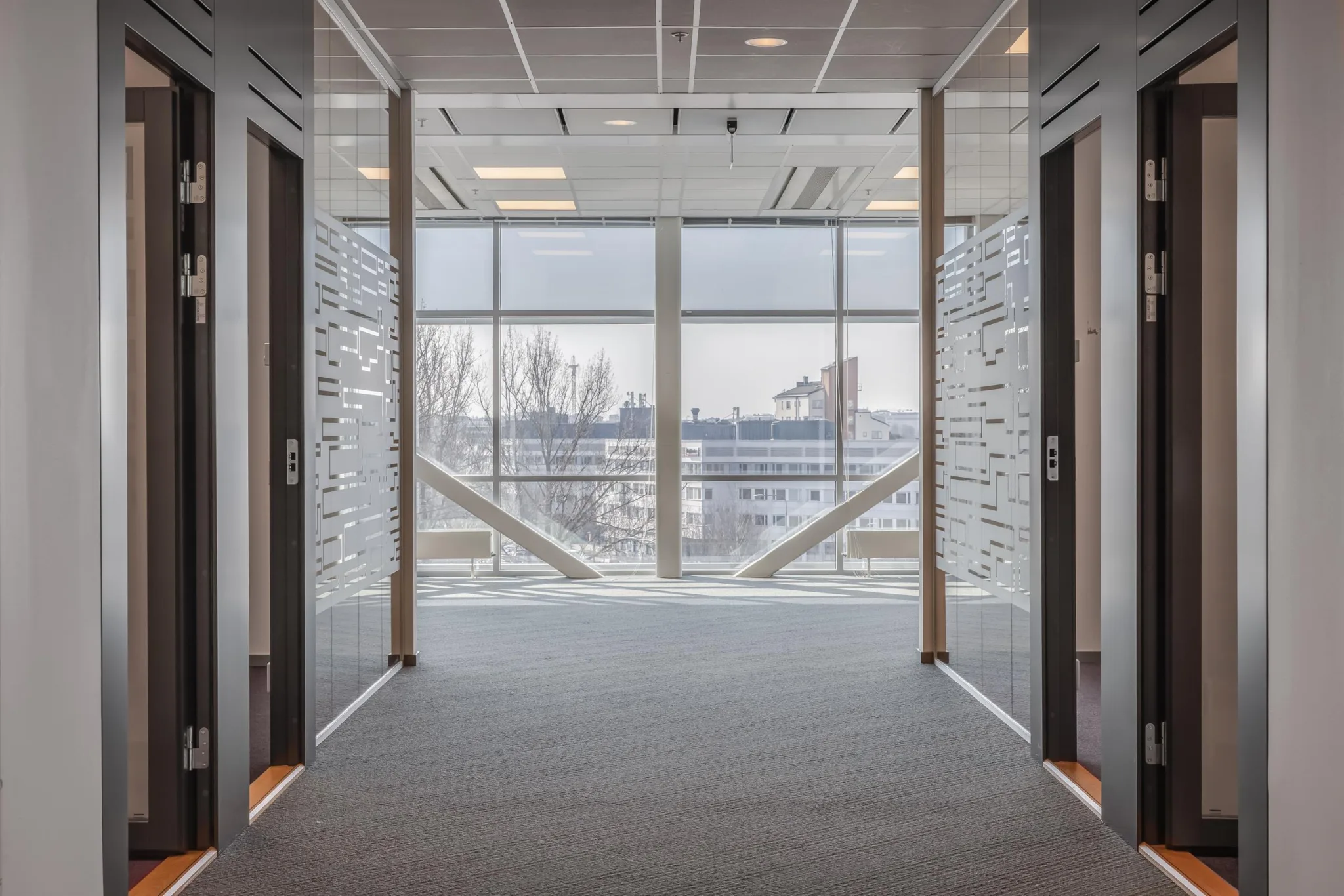 En modern korridor med glasväggar och en utsikt över byggnader genom ett stort fönster.