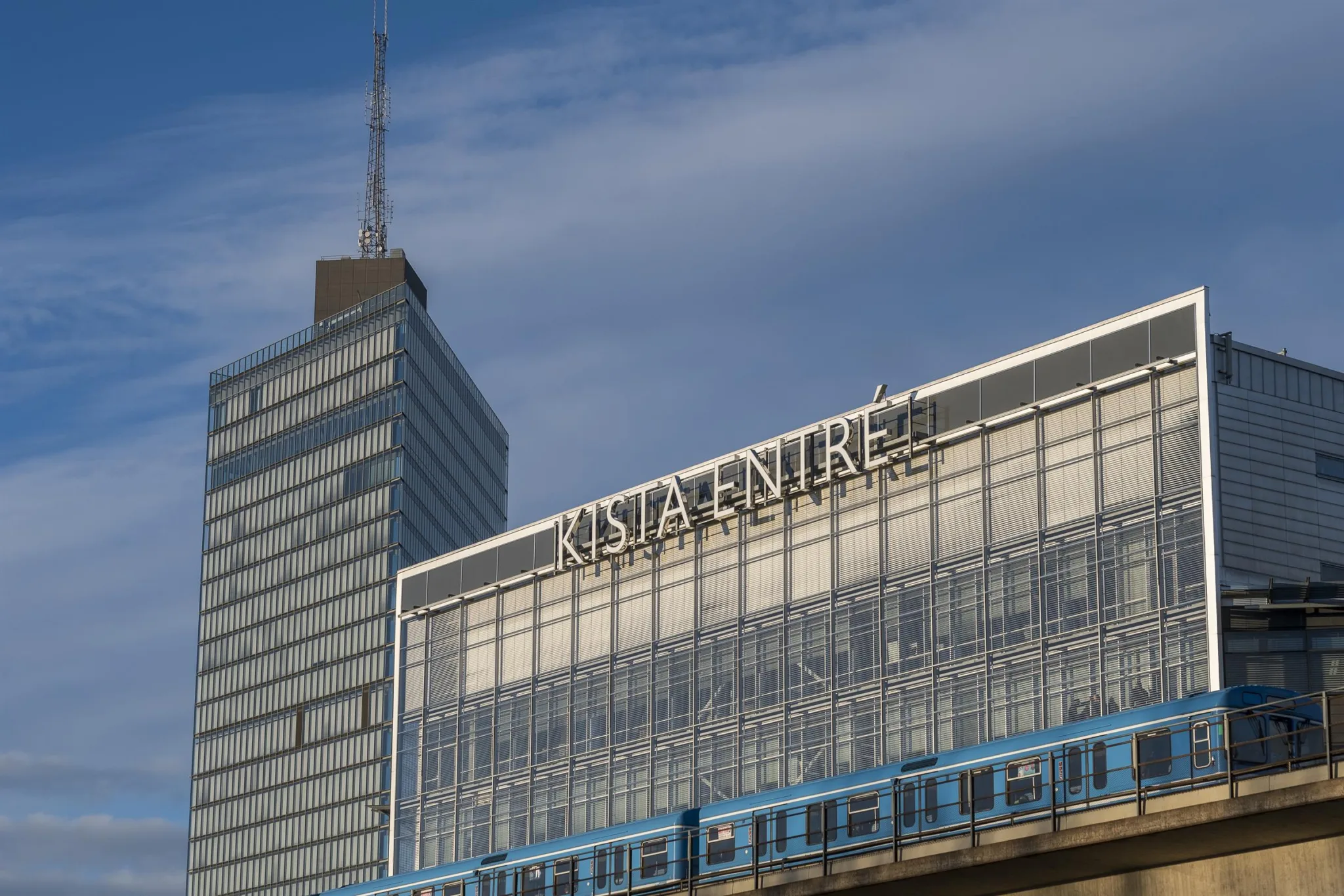 En byggnad med skylten "Kista Entré" på fasaden under en blå himmel.